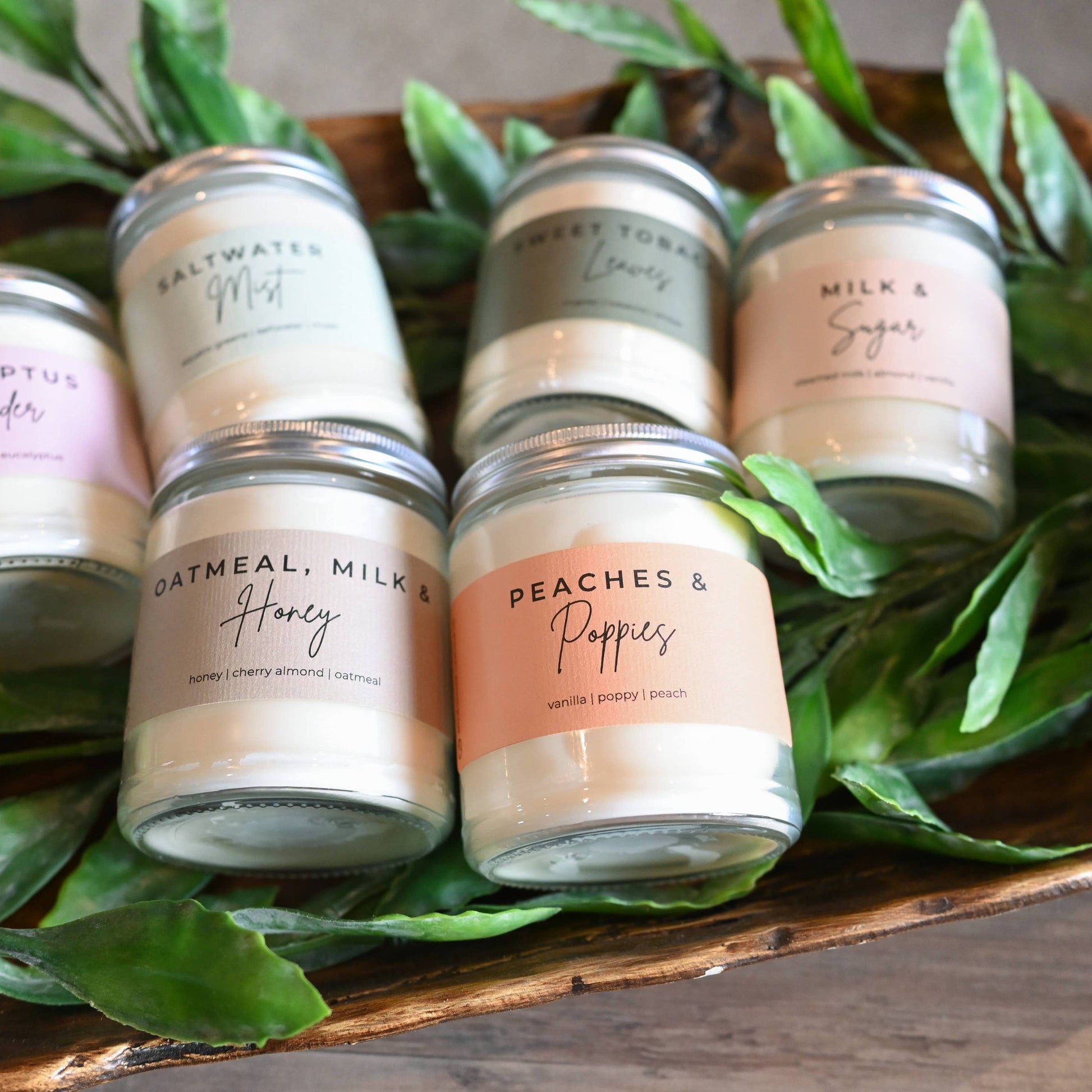Set of small candles with labels on a wooden tray surrounded by green leaves