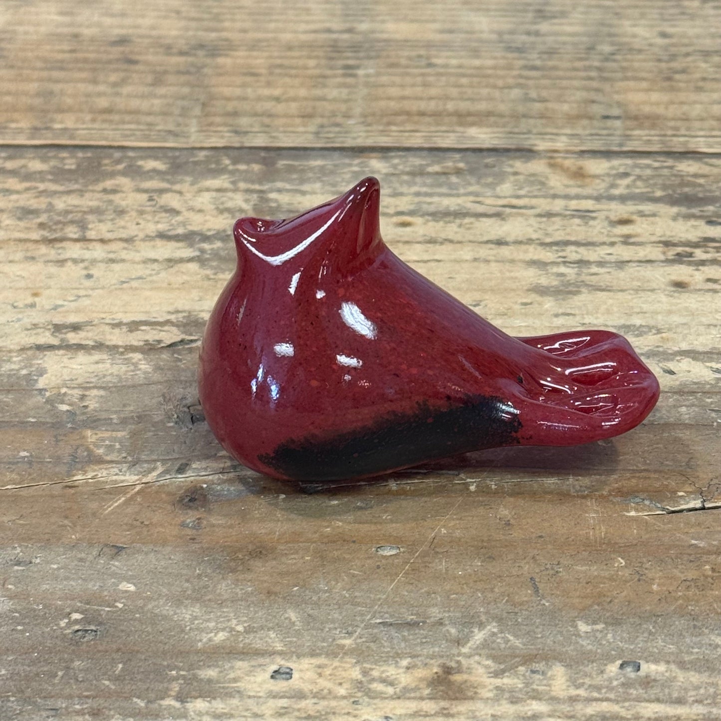 A glossy red ceramic bird figurine, shaped like a cardinal with its beak open, resting on a rustic wooden surface.
