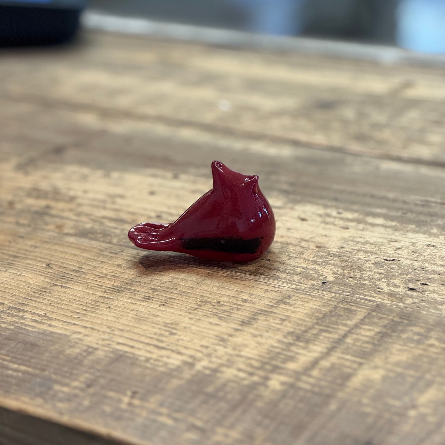 A small glossy red bird figurine, resembling a cardinal, resting on a rustic wooden tabletop.