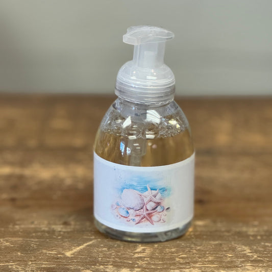 Clear pump bottle with white label. Label has seashells and beach scene