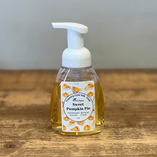 A bottle of Sweet Pumpkin Pie hand foam with a white pump dispenser and a white label decorated with pumpkin illustrations, sitting on a wooden tabletop.