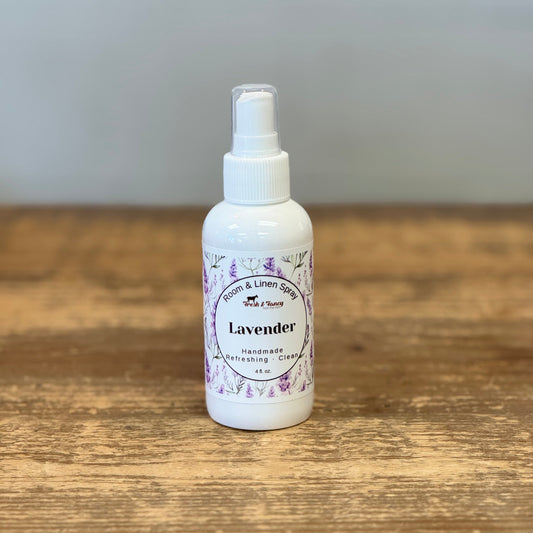 A small white spray bottle labeled 'Lavender' with a white pump top, standing on a rustic wooden surface against a soft gray background.