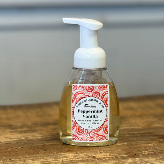 A bottle of Peppermint Vanilla hand soap with a white pump dispenser, sitting on a rustic wooden table against a blurred gray background.